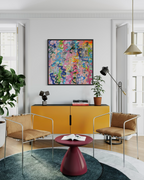 Modern living room with yellow cabinet, colourful abstract art, and stylish chairs.
