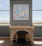 Dining room with a wicker table and chairs, colourful abstract painting on the wall, and large windows.