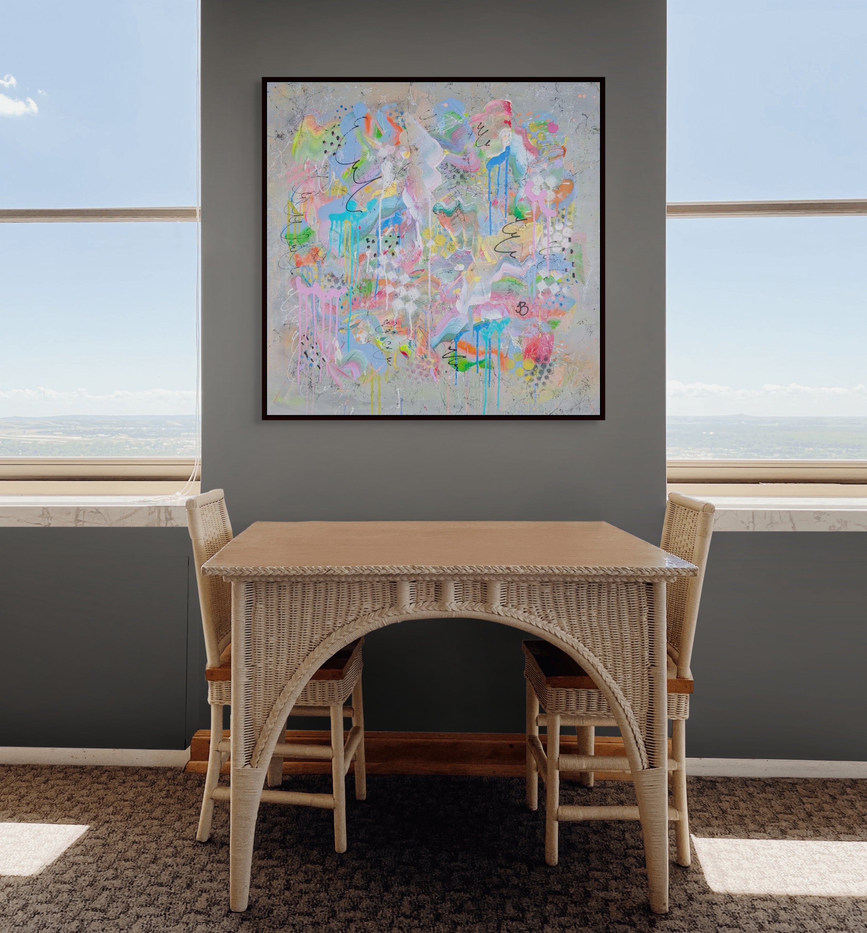 Dining room with a wicker table and chairs, colourful abstract painting on the wall, and large windows.