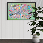 Colorful abstract painting in a black frame on a white wall with a plant to the right.